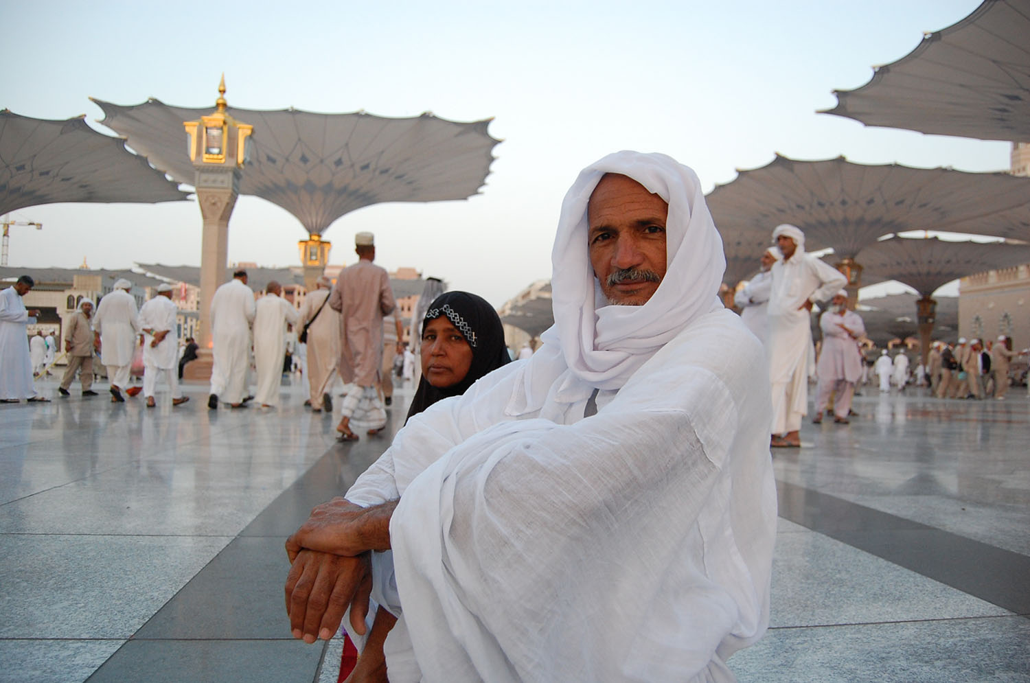 A pilgrim and his wife in the exterior courtyard of the Masjid al-Nabi. Giant retractable umbrellas shield them from the sun.